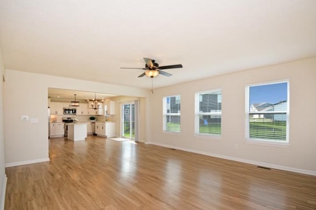 unfurnished living room with wood finished floors, visible vents, baseboards, and ceiling fan with notable chandelier
