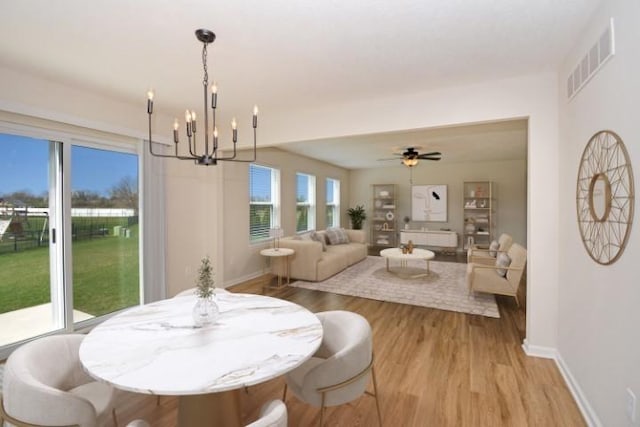 dining area with light wood-type flooring, baseboards, visible vents, and ceiling fan with notable chandelier