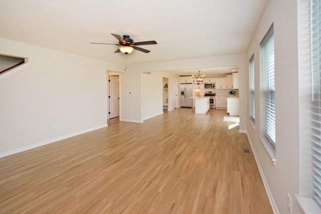 unfurnished living room with baseboards, light wood finished floors, and ceiling fan with notable chandelier
