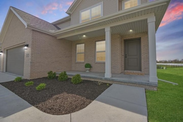 doorway to property featuring brick siding, a yard, an attached garage, and covered porch