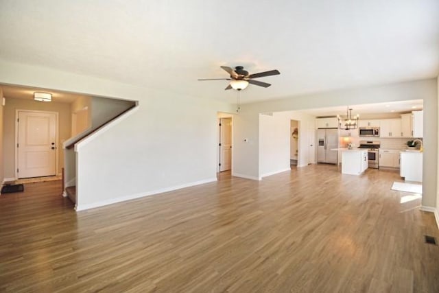 unfurnished living room with wood finished floors, baseboards, and ceiling fan with notable chandelier