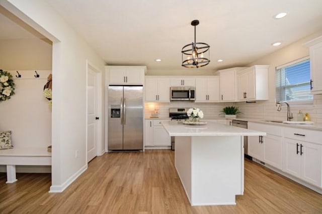 kitchen with light countertops, a kitchen island, decorative backsplash, light wood-style flooring, and appliances with stainless steel finishes