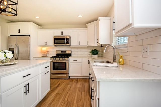 kitchen with tasteful backsplash, a sink, light wood-style floors, stainless steel appliances, and white cabinetry