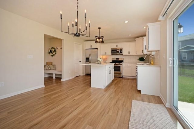 kitchen featuring stainless steel appliances, light countertops, a kitchen island, tasteful backsplash, and a notable chandelier