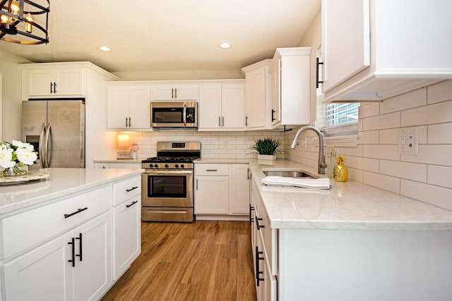 kitchen featuring light wood-type flooring, stainless steel appliances, white cabinets, and a sink