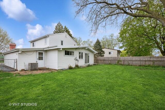 rear view of house with a lawn, fence, central air condition unit, and a chimney