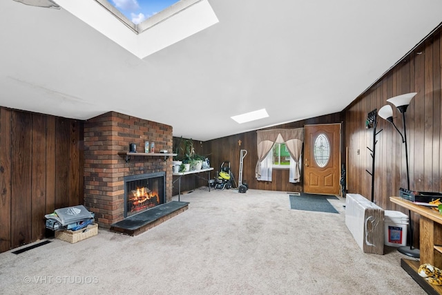 carpeted living area with wooden walls, a skylight, and a fireplace
