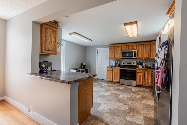 112 E Peru St, Princeton, IL 61356 - kitchen featuring stainless steel appliances, a peninsula, brown cabinetry, and dark countertops