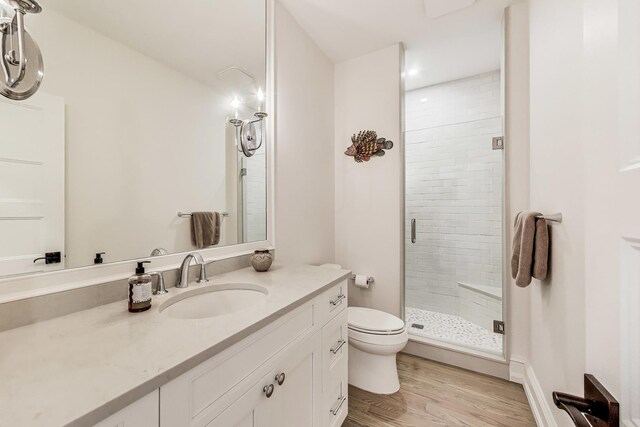 bathroom with toilet, wood finished floors, vanity, and a stall shower