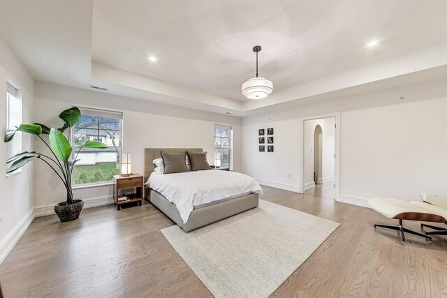 bedroom with arched walkways, a raised ceiling, baseboards, and multiple windows
