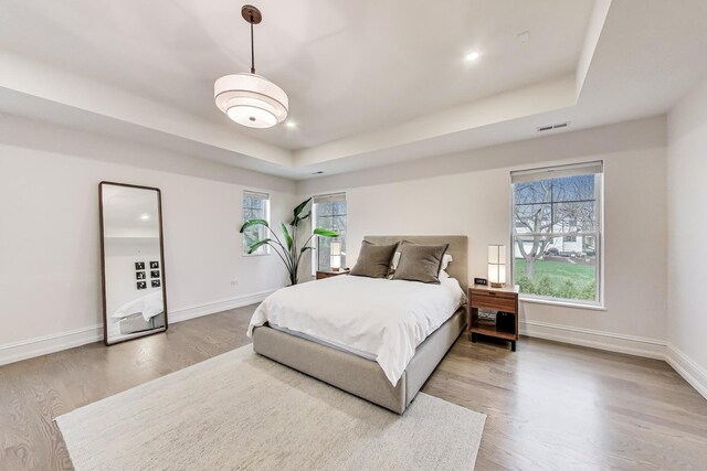 bedroom featuring baseboards, wood finished floors, a tray ceiling, and visible vents