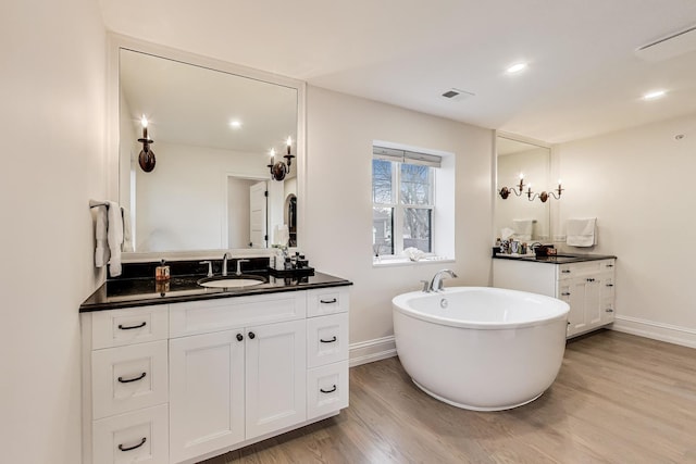 full bath featuring two vanities, baseboards, wood finished floors, and a sink