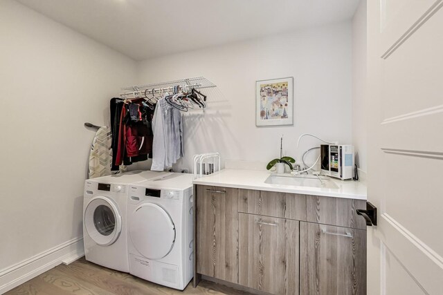 washroom with a sink, cabinet space, light wood-style flooring, washing machine and dryer, and baseboards