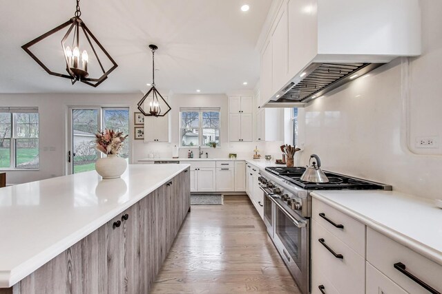 kitchen featuring a sink, light wood-type flooring, wall chimney exhaust hood, light countertops, and range with two ovens