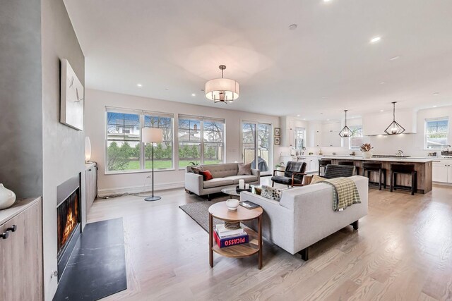 living area featuring baseboards, recessed lighting, a glass covered fireplace, and light wood-type flooring