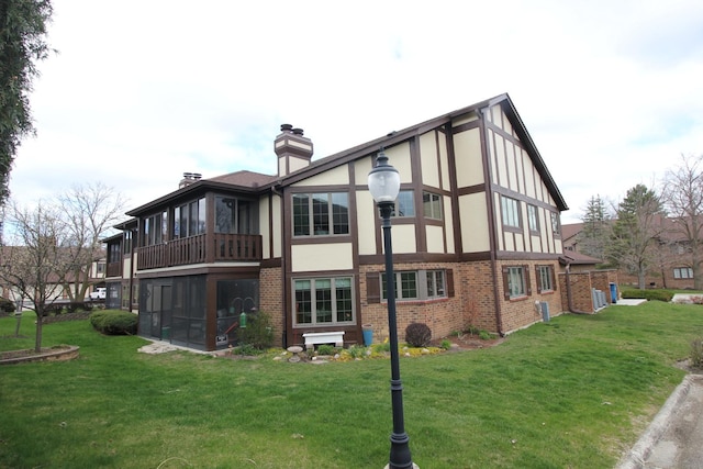 rear view of property with a yard, a sunroom, a chimney, and brick siding