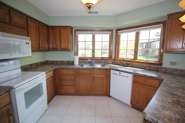 kitchen with a sink, brown cabinetry, white appliances, and dark countertops