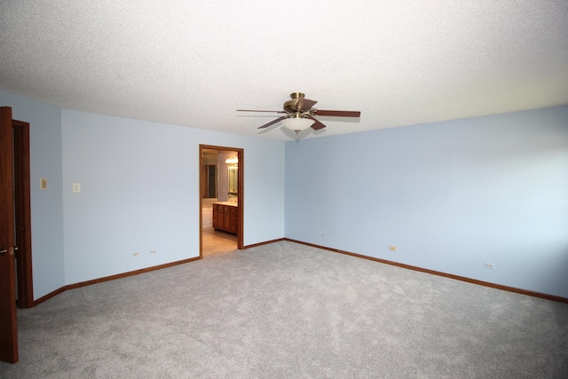 spare room featuring ceiling fan, a textured ceiling, light colored carpet, and baseboards