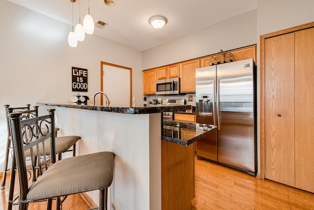 kitchen featuring stainless steel appliances, a peninsula, light wood-type flooring, visible vents, and a breakfast bar