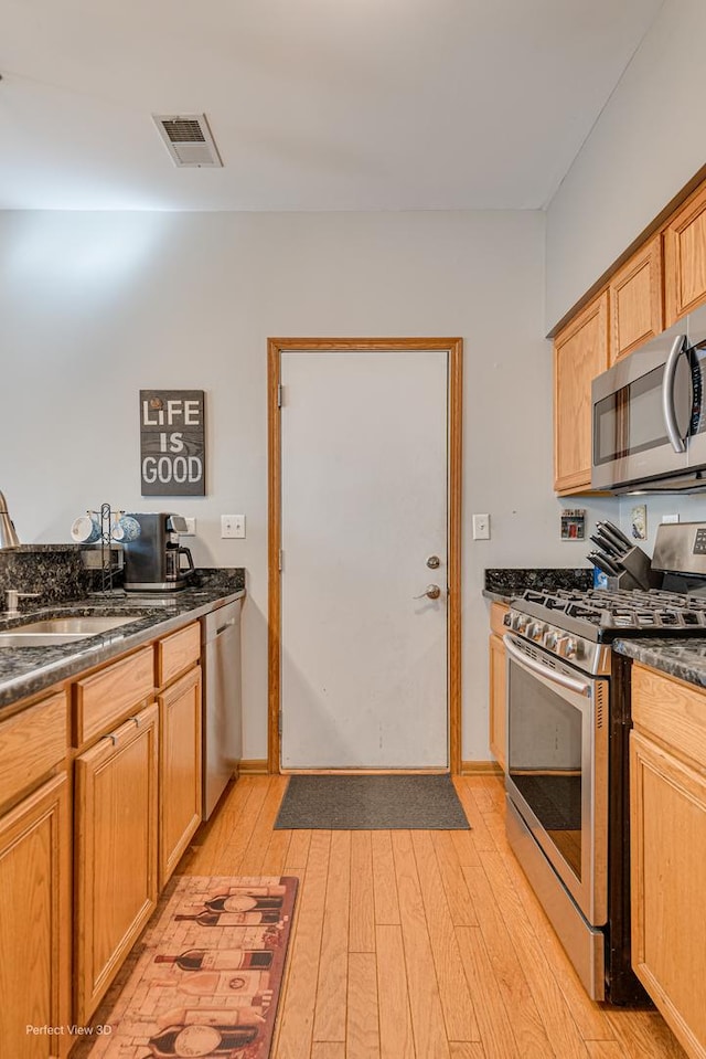 kitchen featuring dark countertops, a sink, light wood-style flooring, appliances with stainless steel finishes, and visible vents