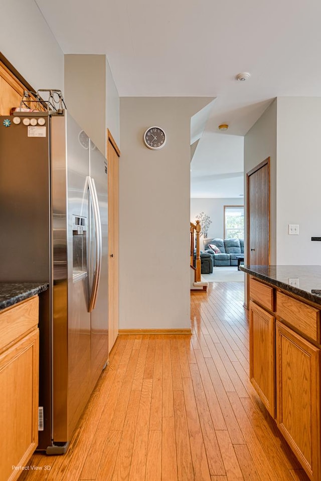 kitchen with light wood finished floors, dark stone countertops, brown cabinetry, stainless steel refrigerator with ice dispenser, and open floor plan
