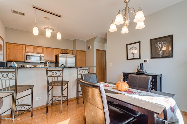dining room featuring light wood-style flooring, baseboards, visible vents, a notable chandelier, and lofted ceiling