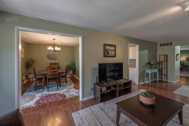living room with wood finished floors, visible vents, baseboards, and an inviting chandelier