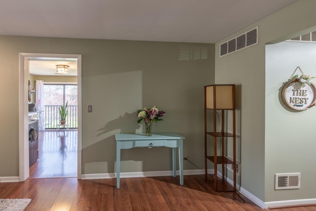 hallway with wood finished floors, visible vents, and baseboards