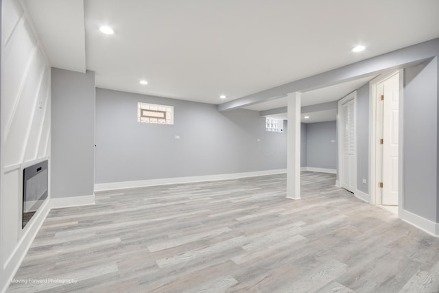 basement featuring light wood-style floors, baseboards, a glass covered fireplace, and recessed lighting