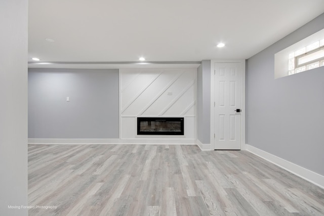 basement featuring baseboards, light wood finished floors, a glass covered fireplace, and recessed lighting
