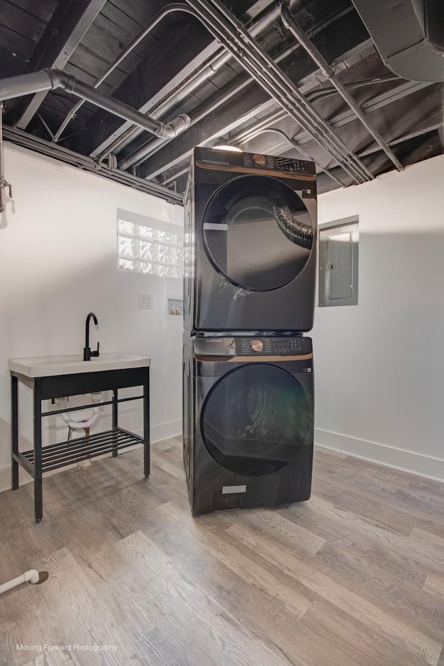 washroom with baseboards, wood finished floors, stacked washer / drying machine, and electric panel
