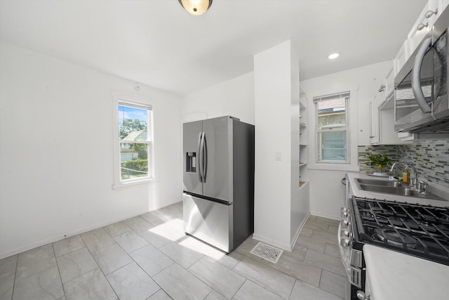 kitchen with visible vents, a sink, stainless steel appliances, decorative backsplash, and baseboards