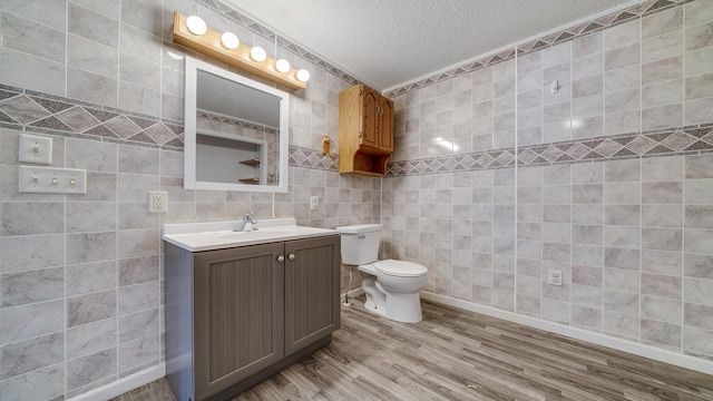 bathroom featuring vanity, a textured ceiling, toilet, tile walls, and wood finished floors