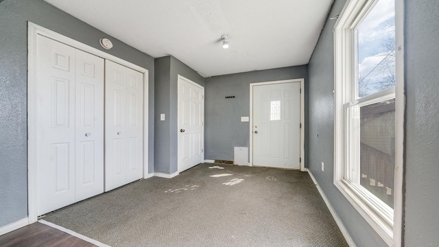 foyer entrance featuring baseboards and dark colored carpet