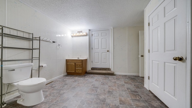 bathroom with vanity, baseboards, a textured ceiling, toilet, and stone finish floor