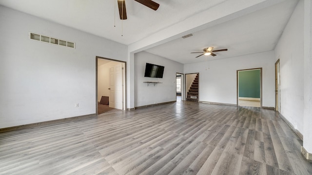 unfurnished living room with stairway, visible vents, wood finished floors, and ceiling fan