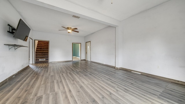 unfurnished living room featuring a ceiling fan, visible vents, wood finished floors, stairs, and baseboards