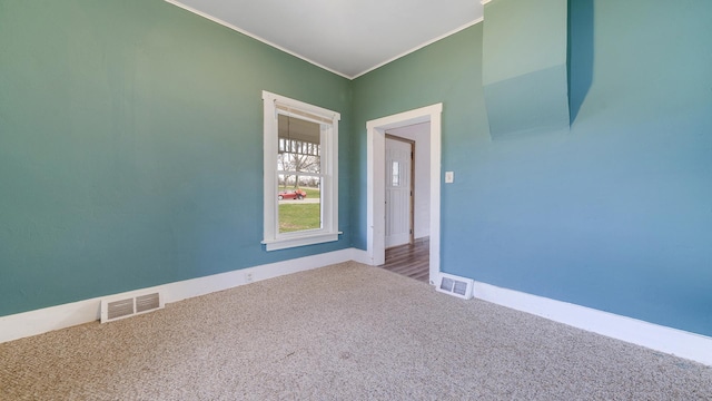spare room with carpet, visible vents, baseboards, and crown molding
