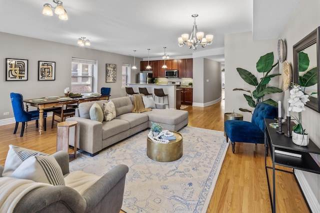 living area featuring light wood-style floors, a notable chandelier, and baseboards