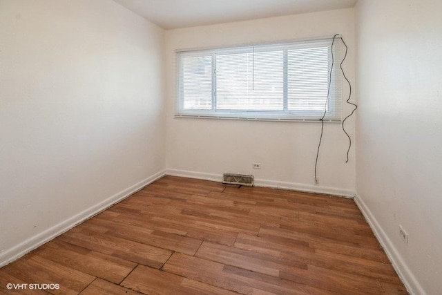empty room with wood finished floors, baseboards, and visible vents