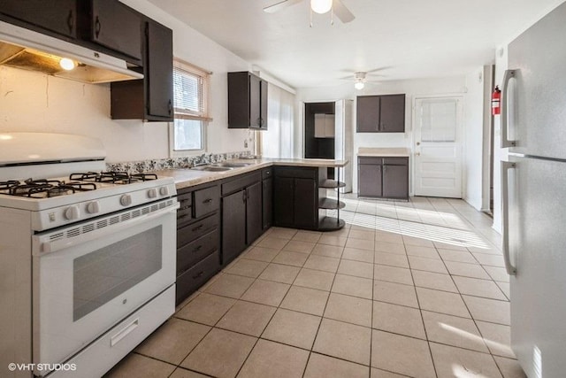 kitchen with freestanding refrigerator, white gas range oven, a ceiling fan, under cabinet range hood, and a sink