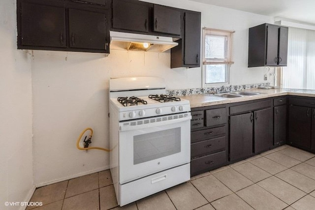 kitchen featuring light tile patterned floors, white range with gas stovetop, under cabinet range hood, light countertops, and a sink