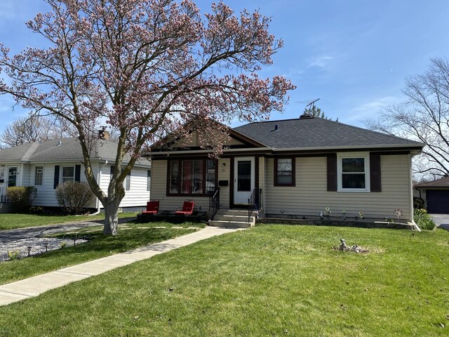 bungalow-style home featuring a front lawn, roof with shingles, and entry steps