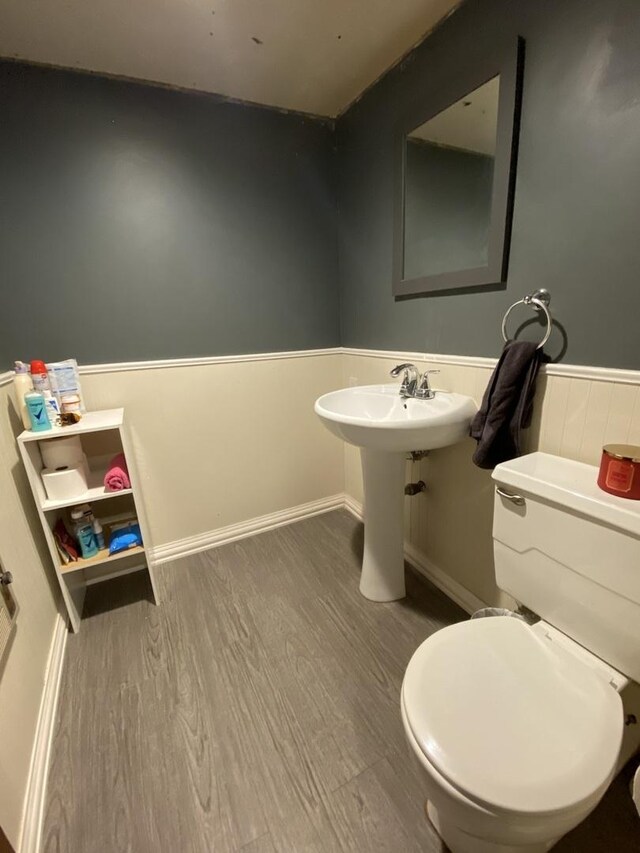half bathroom with wainscoting, wood finished floors, and toilet