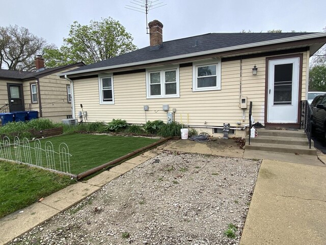 back of property with entry steps, a chimney, a yard, and a patio area