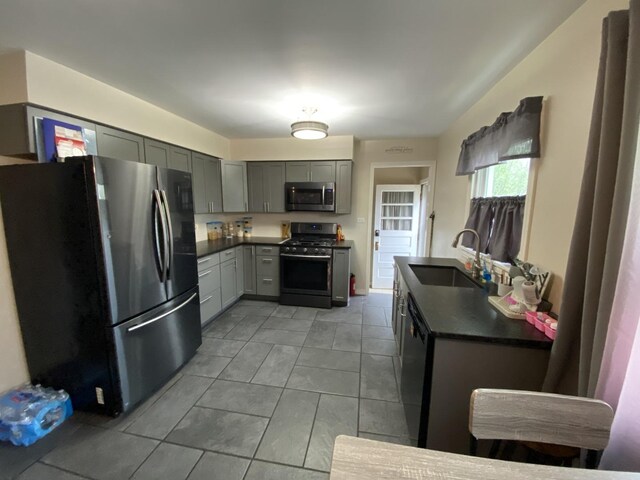 kitchen featuring dark countertops, a sink, gray cabinetry, light tile patterned floors, and stainless steel appliances