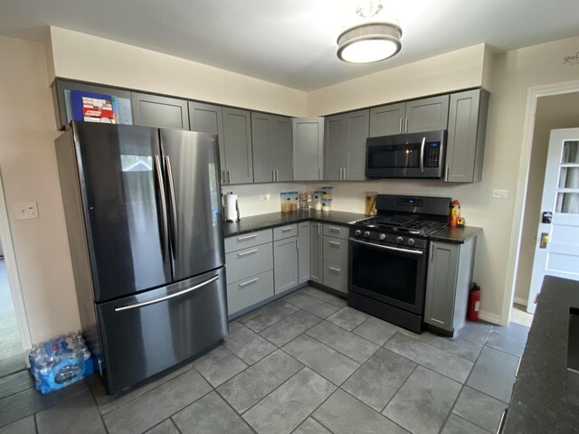 kitchen featuring gray cabinetry, dark countertops, appliances with stainless steel finishes, and light tile patterned floors