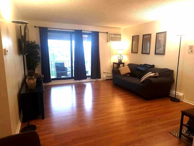 living area with baseboard heating, wood finished floors, a textured ceiling, and a wall unit AC
