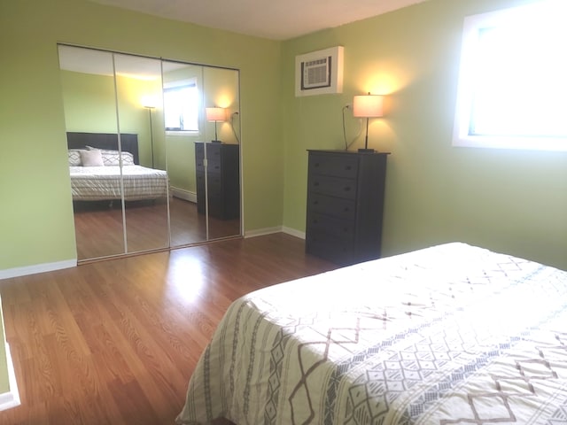 bedroom with baseboards, wood finished floors, a wall mounted AC, and a closet
