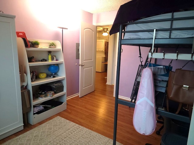 bedroom featuring stacked washer / drying machine, wood finished floors, and electric panel